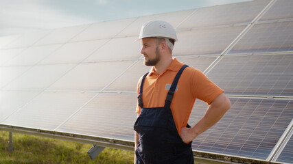 Portrait of ecological expert industrial worker in uniform standing by solar panels installation. Construction of solar station. Workman. Clean energy production. Green energy. Ecological solar farm.