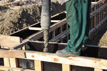 Concrete footing construction. A building contractor is pouring a concrete slab into a timber concrete formwork for a concrete foundation of a new house.