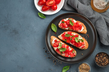 Italian bruschetta with tomatoes, cream cheese and basil on a dark gray-blue background.
