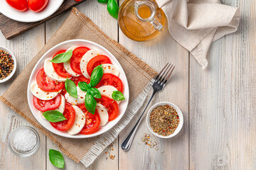 Italian caprese salad with tomatoes, mozzarella cheese and basil in a plate on a beige wooden background.