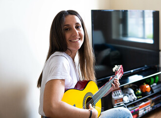 Music Concepts. Latin girl playing guitar. Latin girl relaxing with music. Latin woman have a happy lifestyle. Beautiful Latin girl playing guitar at home.
