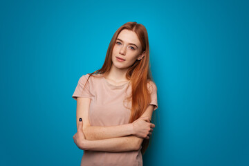 Obraz premium Ginger woman with freckles on a studio wall. Person on blue background. Woman outfit. Fashionable girl smiling.