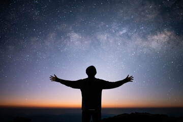 Silhouette of young traveler wearing sweater raise both hands and watched the star and milky way alone on top of the mountain. He enjoyed traveling and was successful when he reached the summit.