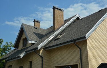 A close-up of a double complex roof of a brick house construction covered with gray asphalt...