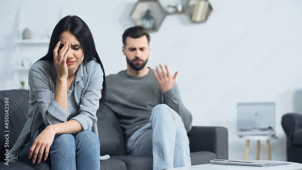 Wall mural upset woman crying near blurred and displeased boyfriend quarrelling at home