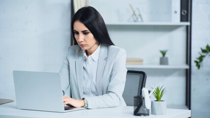 Obraz na płótnie Canvas brunette and worried businesswoman using laptop in office