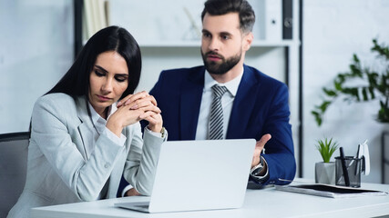 sad businesswoman looking away near blurred businessman quarrelling in office