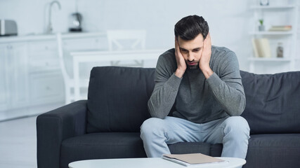 Fototapeta premium tensed man looking at folder and touching face at home