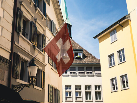 swiss flag in zurich city centre with old buildings and blue sky - swiss flag in switzerland old town