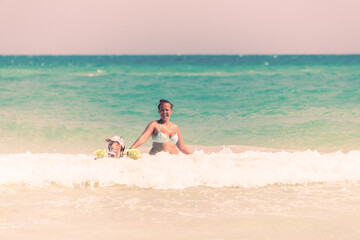 Fototapeta na wymiar Mom and daughter swim together on the waves, mom teaches daughter to swim