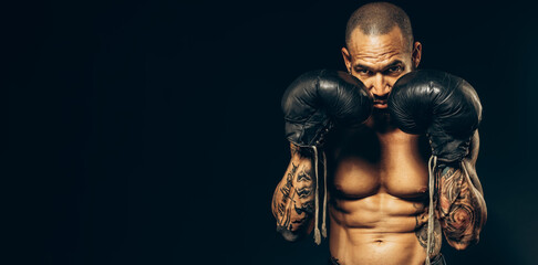 Studio portrait of a muscular boxer in gloves on a dark background. Advertising banner for boxing or martial arts school. A Latino or Cuban with a naked torso in old boxing gloves.