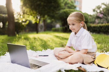 happy caucasian kid has online lesson on laptop during coronavirus covid-19 pandemic and lockdown