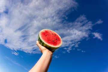 Watermelon in one hand. Cut off halved watermelon in the blue sky. Health fruit with blue cloudy background.