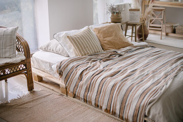 Fototapeta na wymiar Cozy bedroom. Bed with pillows and striped blanket at cozy light bedroom