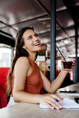 A charming girl is sitting in a cafe, drinking a drink, making notes in a notebook