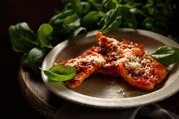 Cooked ravioli with tomato sauce and cheese on a wooden table with green basil