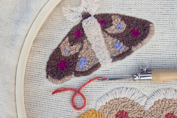 Closeup of embroidered moth on canvas in a hoop with punch needle closeup and brick-red thread...