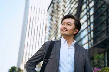 successful asian corporate businessman walking on downtown street in modern city