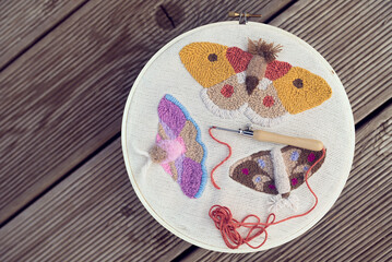 Top view of three embroidered multicolored butterflies on two-thread cloth in a hoop with punch...