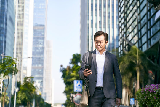 Asian Business Man Looking At Mobile Phone While Walking In Street