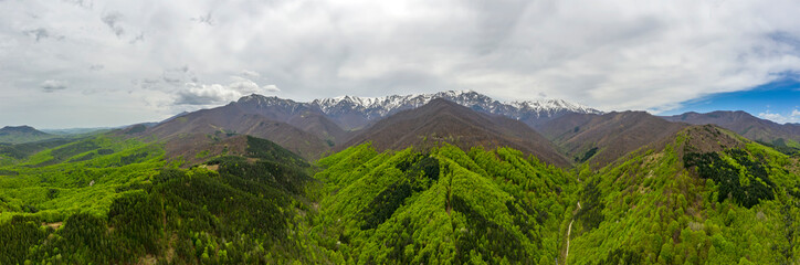 Amazing panorama in spring with snow-capped mountains and hills with green forest.