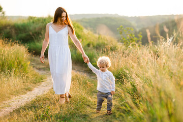 Fototapeta na wymiar Mom and son walk holding hands in the summer field