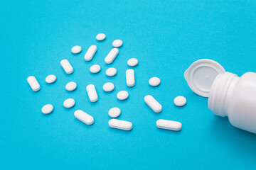 Global Pharmaceutical Industry and Medicinal Products - White Pills or Tablets Scattered from the Pill Container, Lying on Blue Background