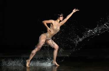young beautiful woman of Caucasian appearance with long hair dances in drops of water on a black...