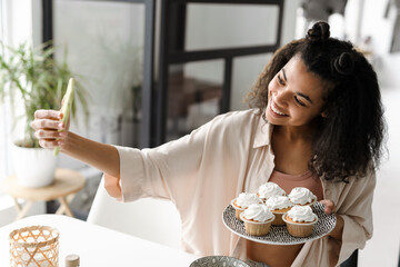 Black young woman taking selfie photo on mobile phone with muffins