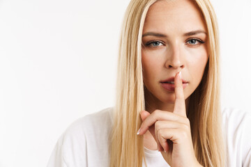 Young blonde woman in t-shirt showing silence gesture at camera