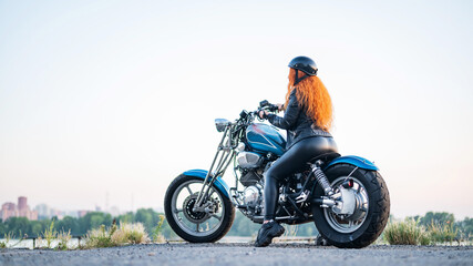 Rear view of red-haired curly woman in helmet on motorcycle outdoors.