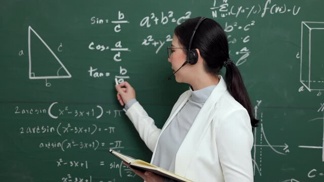 Young asian teacher woman teaching holding chalk wearing headset video conference with student looking camera. Female teacher training the mathematics in classroom blackboard online course.