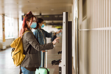 Young multiracial women in face masks buying ticket at train station