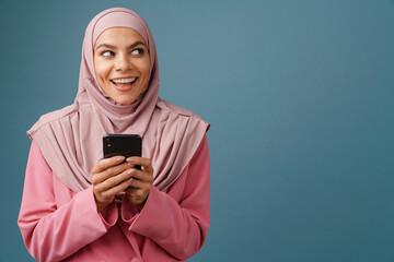 Young muslim woman in hijab smiling while using mobile phone