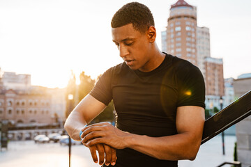 Black young sportsman using smartwatch while working out