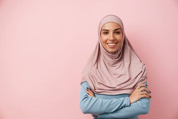 A smiling muslim woman wearing pink hijab standing with crossed arms