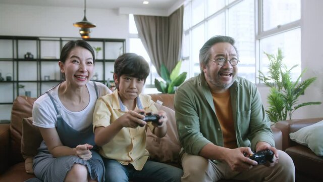 family quality time ,asian parent and son sit relax playing game console together laugh joyful smiling on sofa couch in living room at home,asian family homs isolation quarantine ideas concept