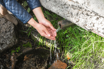 a woman takes cold spring water in her hands to quench her thirst
