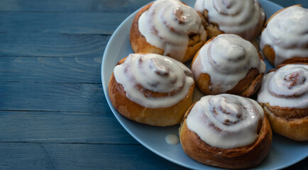 Homemade swirled rosy buns covered with white cream on a blue plate on the right on a blue wooden background