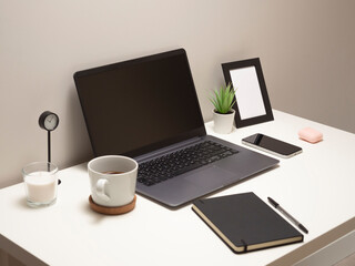 Fototapeta premium Picture of laptop on a white table with a mug a clock a small bush a notebook a phone a picture frame and a headphone case