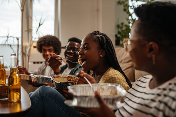 Group of young friends enjoying takeout food at home during weekend