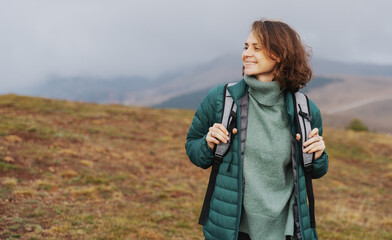Beautiful cheerful young woman with a backpack walking in the autumn hills enjoying the fresh air...