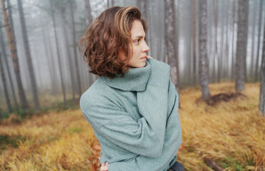 Beautiful stylish sensual elegant young woman standing in green sweater in foggy autumn pine forest