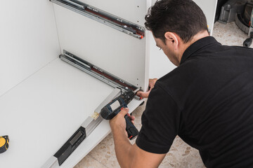 Man fixing kitchen cabinet rails with a drill