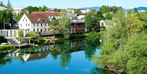 Fototapeta premium Novo Mesto, Slovenia - May 9. 2017: View over river Krka on village against summer sky