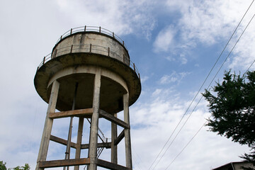 Stock photo of a old rusty yellow painted water tank tower under blue sky with white clouds at the middle of the Kolhapur Maharastrian Village area. Attached with iron stairs and plastic pipelines.