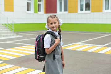 a cute little schoolgirl in a school uniform holds a backpack and smiles at the camera. Return to school. Knowledge Day