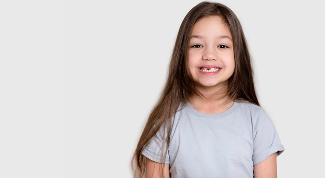 Portrait of a beautiful happy laughing child girl, close-up. Happy childhood concept, smiling. Little girl in white or grey blank t-shirts. The tooth is growing in the wrong place.