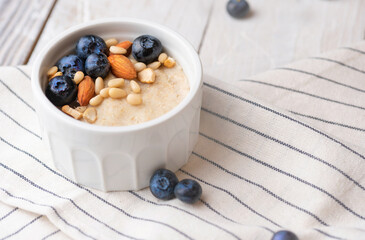 Sweet oat flakes porridge decorated with blueberry, almond, pine nuts in a ceramic white bowl on...