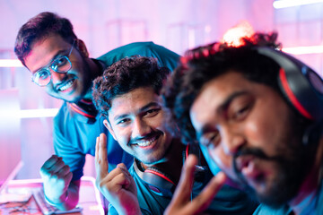 Team of professional gamers with headphones taking selfie by holding camera during esports video gaming tournament.